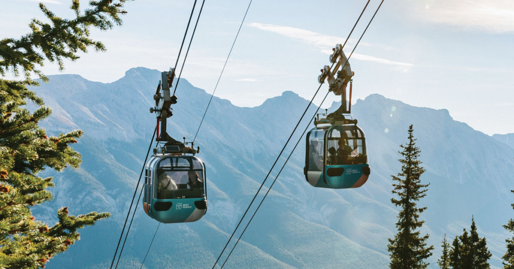 Four-passenger Banff Gondola cabin ascending Sulphur Mountain with the snow-capped Canadian Rocky Mountains and Bow Valley in the background.